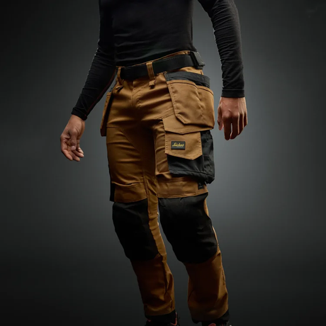 Person wearing a brown and black multi-pocket work pants on a dark background